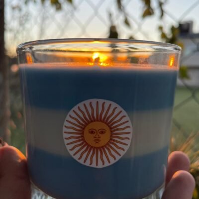 vela-albiceleste-aromatica-sol-de-mayo-svelas Primer plano de vela aromática celeste y blanca con el Sol de Mayo de Svelas para decoración del mundial.
