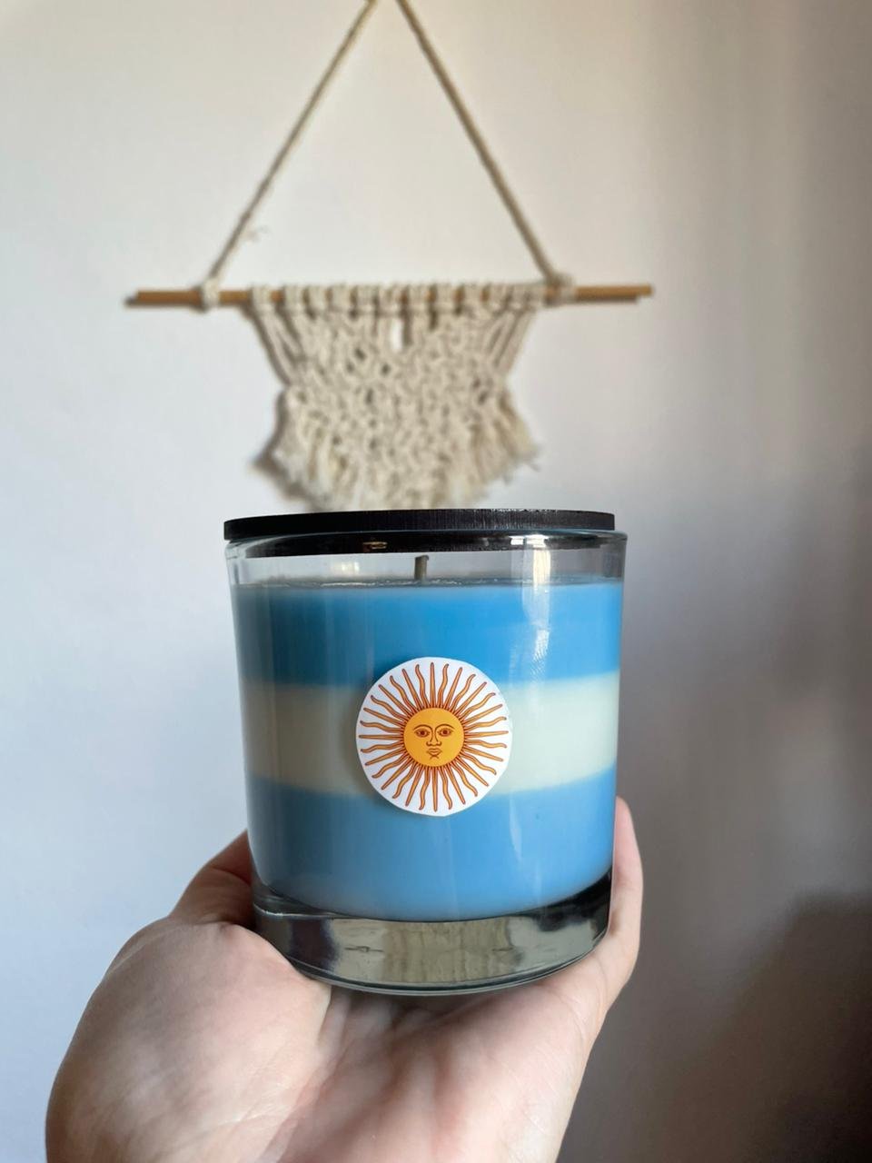 Vela decorativa con colores de Argentina y tapa de madera en un ambiente con decoración de macramé.