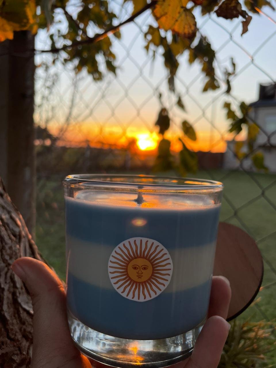 Vela artesanal con colores de la bandera argentina sostenida frente a un atardecer en el campo de Entre Ríos